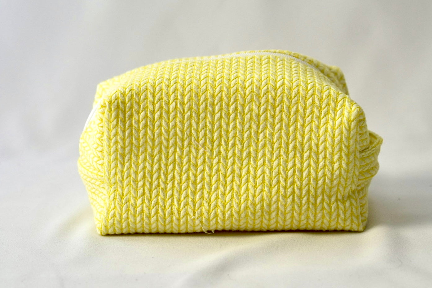 Back view of a bright yellow cosmetic pouch with a soft, quilted knit-pattern fabric. The bag features a structured, padded shape with a clean, minimalist design and no visible front label.