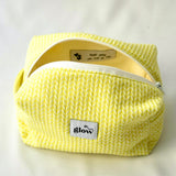 Open view of a bright yellow cosmetic pouch with a soft, quilted knit-pattern fabric and a white zipper. The bag reveals a spacious interior with a sewn-in label featuring a motivational message, combining functionality with an uplifting detail.