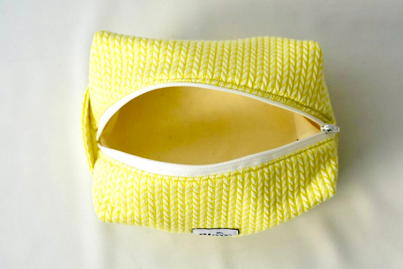 Open cosmetic pouch in bright yellow with a soft, quilted knit-pattern fabric and a white zipper. The bag reveals a spacious, light-colored interior, highlighting its practical design for everyday essentials.