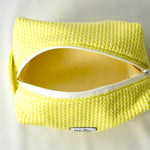 Open cosmetic pouch in bright yellow with a soft, quilted knit-pattern fabric and a white zipper. The bag reveals a spacious, light-colored interior, highlighting its practical design for everyday essentials.