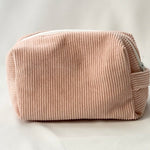 Back view of a blush pink cosmetic pouch made from soft corduroy fabric. The bag features a structured, padded shape with a clean, minimalist design and no visible front label.