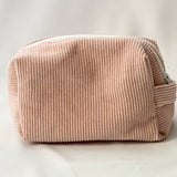 Back view of a blush pink cosmetic pouch made from soft corduroy fabric. The bag features a structured, padded shape with a clean, minimalist design and no visible front label.