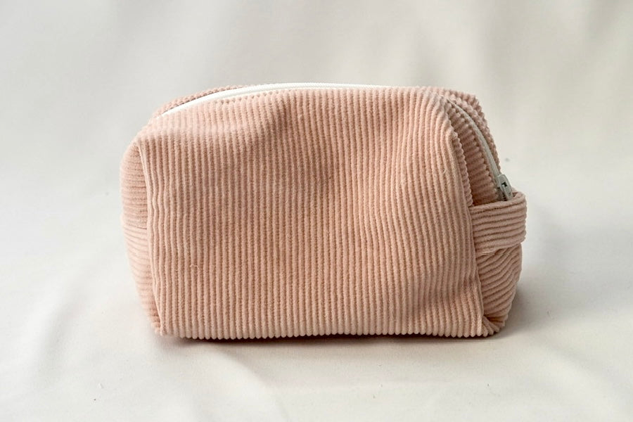Back view of a blush pink cosmetic pouch made from soft corduroy fabric. The bag features a structured, padded shape with a clean, minimalist design and no visible front label.