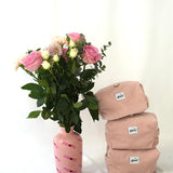 Three blush pink cosmetic pouches made from soft corduroy fabric with “glow” logo labels stacked next to a bouquet of pink and white flowers in a pink vase. A small camera and “glow” stickers are placed in front, creating a soft, feminine and lifestyle-inspired scene.
