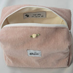 Open view of a blush pink cosmetic pouch made from soft corduroy fabric with a white zipper. The bag reveals a light-colored interior with a sewn-in label that reads “keep going, you can do this,” along with small heart details, combining functionality with an encouraging message.