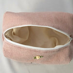 Open cosmetic pouch in blush pink corduroy fabric with a white zipper. The bag reveals a spacious, light-colored interior, highlighting its soft structure and practical design for everyday essentials.