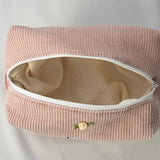 Open cosmetic pouch in blush pink corduroy fabric with a white zipper. The bag reveals a spacious, light-colored interior, highlighting its soft structure and practical design for everyday essentials.