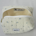 Open view of a soft, quilted cosmetic pouch in light cream fabric with a delicate blue floral pattern. The bag features a white zipper and a spacious interior with a sewn-in label that reads “keep going, you can do this,” alongside small heart icons.