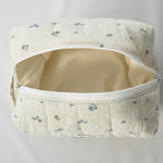 Open cosmetic pouch made of soft, quilted cream fabric with a delicate blue floral pattern and a white zipper. The bag reveals a spacious, light-colored interior designed to hold everyday essentials.