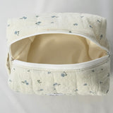 Open cosmetic pouch made of soft, quilted cream fabric with a delicate blue floral pattern and a white zipper. The bag reveals a spacious, light-colored interior designed to hold everyday essentials.