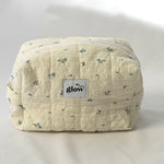 A soft, quilted cosmetic pouch in light cream fabric with a delicate blue floral pattern and a white zipper. The front features a small “glow” logo label. The bag has a structured, spacious shape, perfect for storing everyday essentials.
