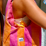 A person wearing a pink and orange striped towel shoulder bag with a yellow drawstring and a visible 'glow' brand label.