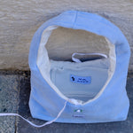 A light blue fleece shoulder bag with a white interior lining, placed on a gray stone surface against a beige stucco wall. The brand name 'KONG PET' is visible on a small blue label inside the bed.