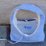 A light blue fleece shoulder bag with a white interior lining, placed on a gray stone surface against a beige stucco wall. The brand name 'KONG PET' is visible on a small blue label inside the bed.