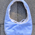 A light blue fabric shoulder bag with a white lining and white tie detail, laid flat on gray concrete pavers.
