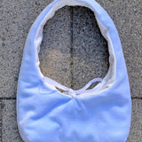 A light blue fabric shoulder bag with a white lining and white tie detail, laid flat on gray concrete pavers.
