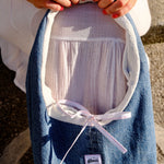 A person holds a denim shoulder bag with a white inner lining and a white ribbon bow. The pouch has a small white label that reads 'glow'.