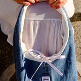 A person holds a denim shoulder bag with a white inner lining and a white ribbon bow. The pouch has a small white label that reads 'glow'.