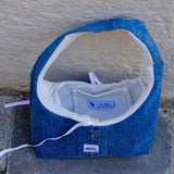 A handmade blue denim shoulder bag with a white cotton lining, resting on a gray stone surface against a textured beige stucco wall. The brand name 'blanco' is visible on a small white patch on the front.
