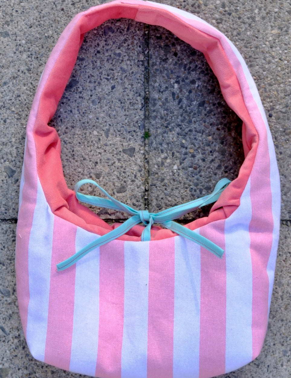 A pink and white striped fabric bag with a coral pink lining and a light blue ribbon bow, placed on a gray concrete surface.
