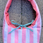 A pink and white striped fabric bag with a coral pink lining and a light blue ribbon bow, placed on a gray concrete surface.