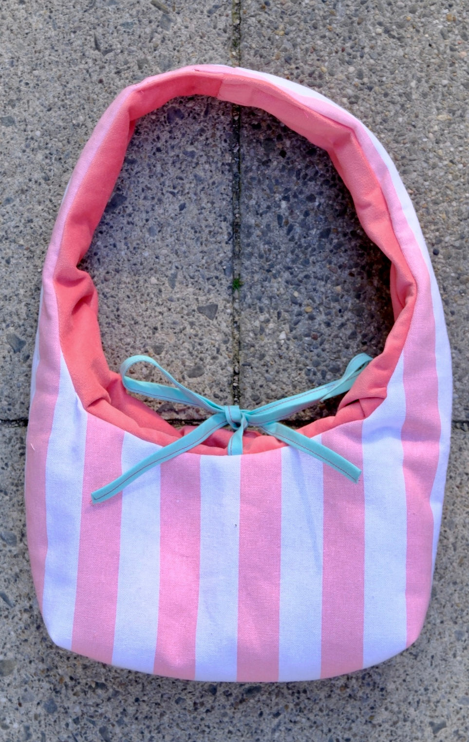A pink and white striped fabric bag with a coral pink lining and a light blue ribbon bow, placed on a gray concrete surface.