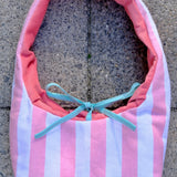 A pink and white striped fabric bag with a coral pink lining and a light blue ribbon bow, placed on a gray concrete surface.