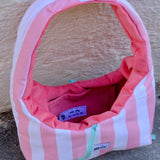 A pink and white striped dog crate with a pink interior, shown outdoors against a textured beige wall and gray pavement. A small sewn label on the front reads glow.