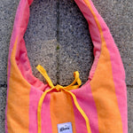 A pink and orange striped bath towel shoulder bag with yellow drawstrings and a small white 'glow' brand label, laid flat on a gray stone surface.