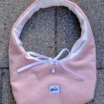 A light pink corduroy baby bib with a white inner lining, white ribbon bow, and a small white button, laid flat on a gray concrete surface. The brand label 'glow' is visible on the front.
