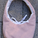 A light pink ribbed fabric headband with a white inner lining and a white ribbon bow, laid flat on a gray concrete surface.