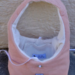 A pink corduroy pet crate or basket-style bed with a white fleece interior, photographed outdoors against a textured beige wall and gray ground. A small sewn label is visible on the front.