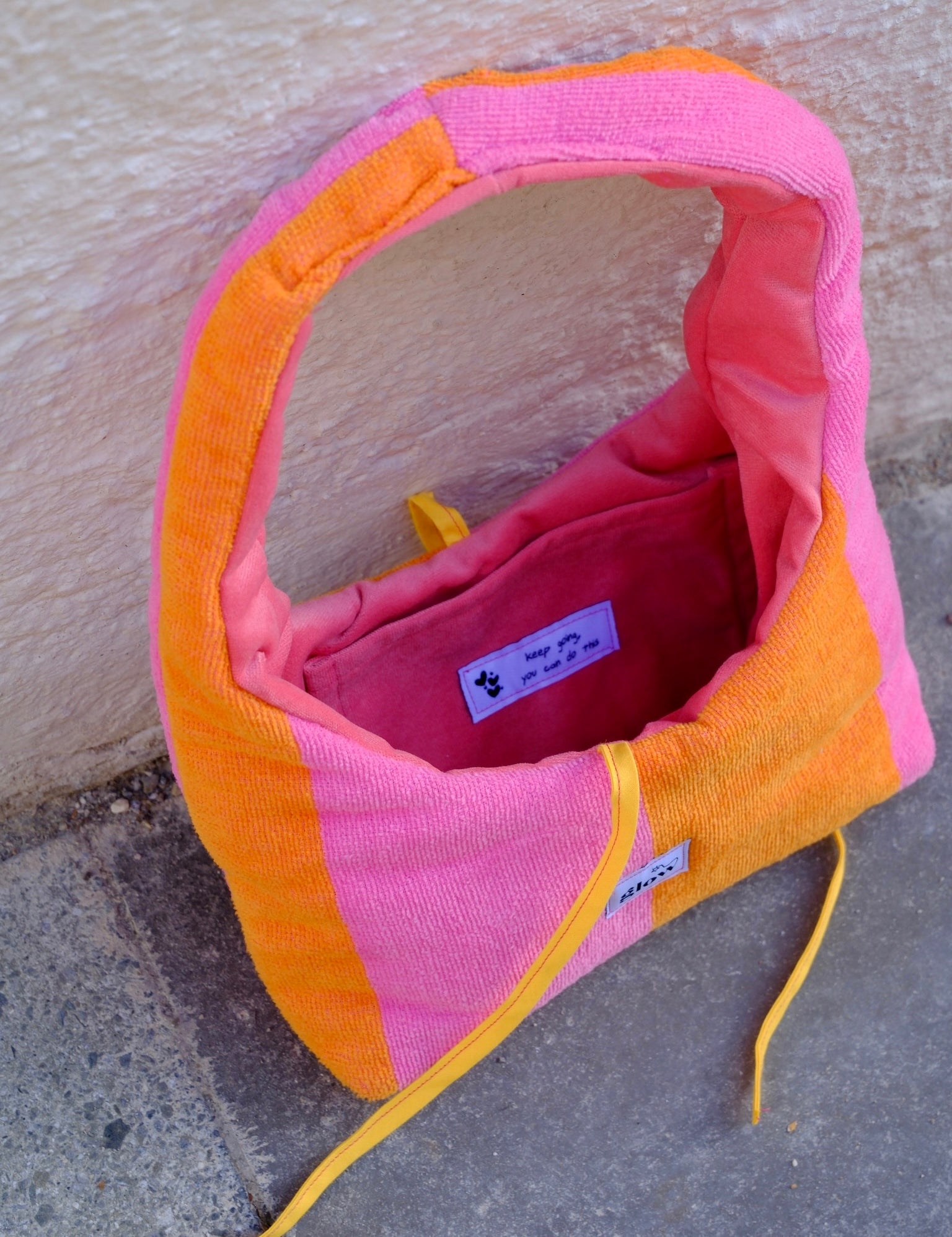A pink and orange striped dog carrier bag made of textured fabric, shown open on a concrete surface against a stucco wall.