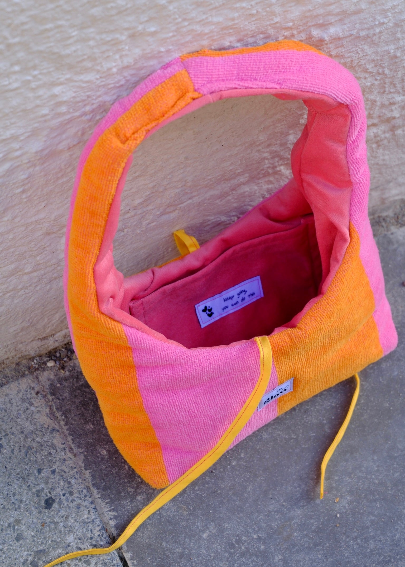 A pink and orange striped dog carrier bag made of textured fabric, shown open on a concrete surface against a stucco wall.