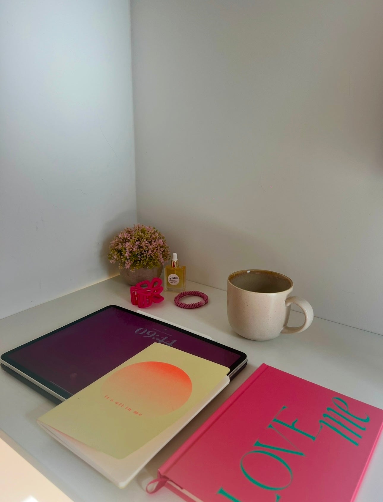 A cozy desk setup with pink journals, a tablet, coffee mug, and flowers — minimalist morning routine and journaling space for self-growth, Glow by Lisa Walter.