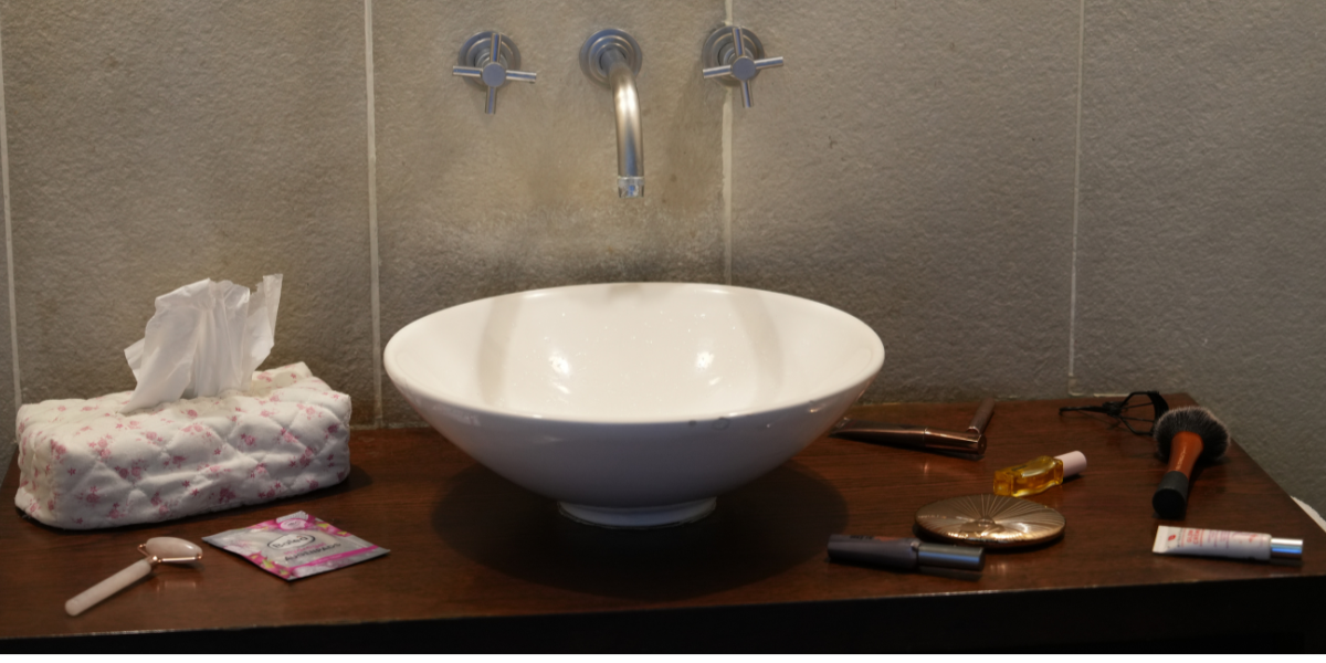 Bathroom sink with skincare and beauty products including facial oil, tissues, and makeup brushes — minimal self-care routine setup, Glow by Lisa Walter.